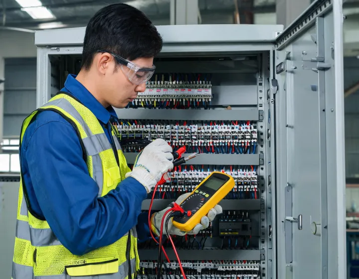 Electrician using a Fluke Multimeter at an industrial control cabinet